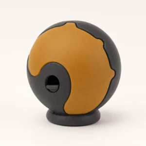 AccessPet Tumble treat-dispensing puzzle ball in amber and charcoal natural rubber with an adjustable dispensing aperture